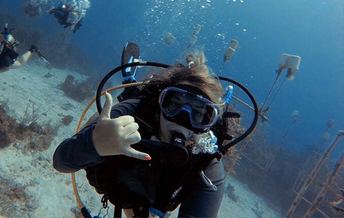 young woman scuba diving, giving hang loose sign